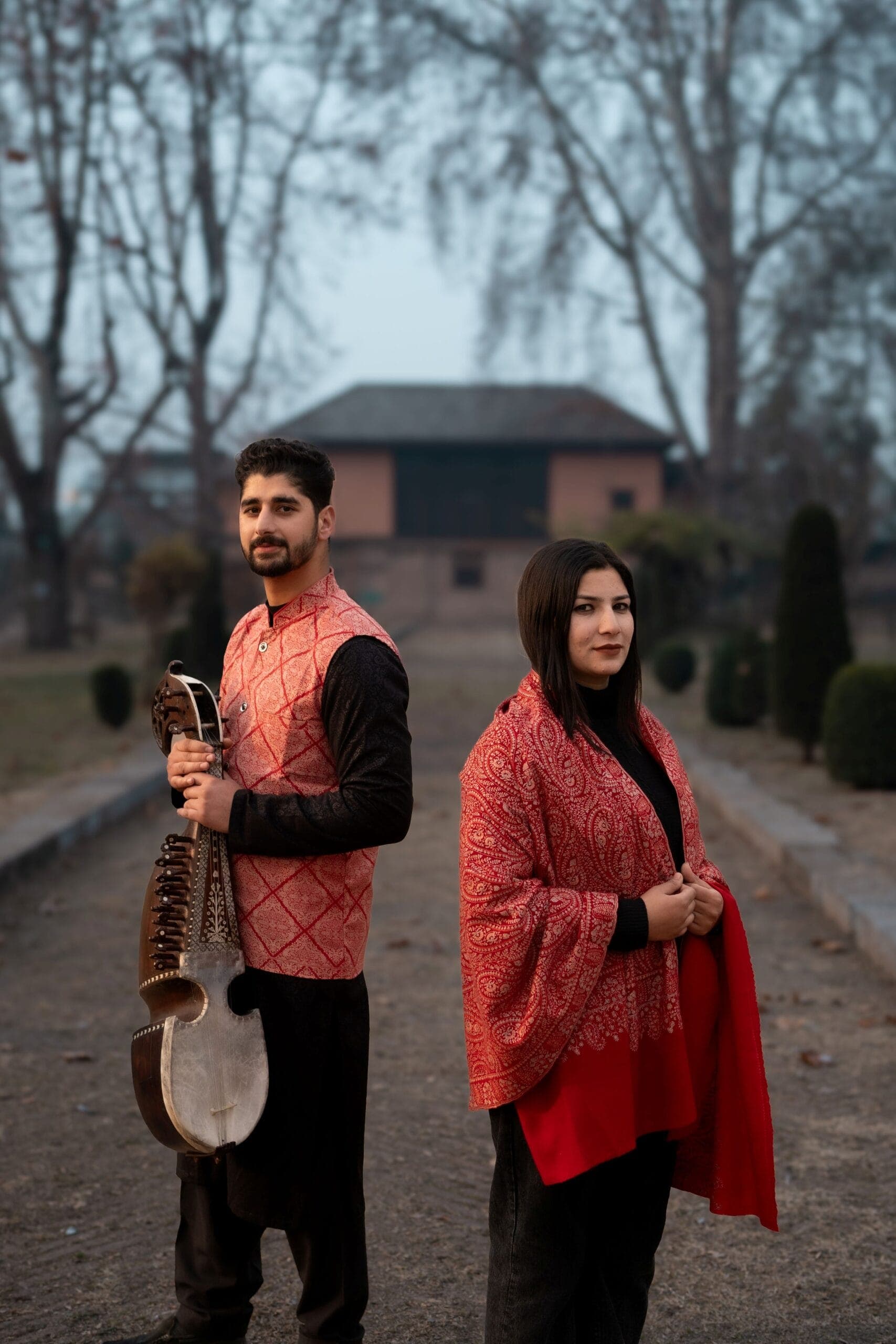 Couple in traditional Kashmiri attire, one holding a sarangi